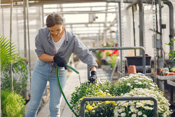 Woman in a greenhouse. Worker pours flowerpoots. Girl in a blue shirt.