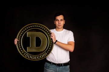 A young guy holds a symbol of the dogecoin coin, a modern currency for exchange and purchases