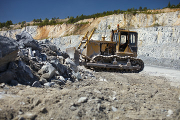 Old rusty bulldozer on the background of the quarry and fragments of stone ore.