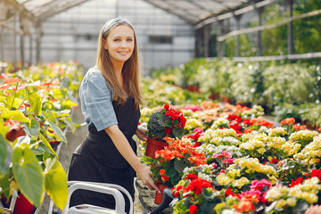 Woman in a greenhouse. Worker pours flowerpoots. Girl in a black apron.