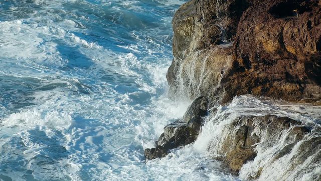 Waves of Ocean Water crash on the rocks of the Volcanic island of Tenerife Clear Blue water of the Sea. Gale the Tide turns into pearl drops and splashes Waves reflect the sun's rays shot URSA 4.6K