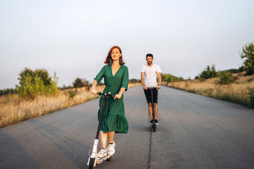 Young happy smiling couple having fun driving electric scooter on the road in the countryside. Content technologies © bedya