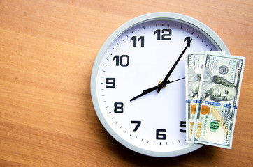 Analog clock and dollars on a wooden background. Banknotes are on the clock and next. Macro. Top and side view. The clock is 20:05, 08:05.  Copy Space
