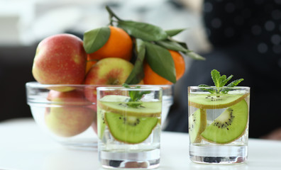 Close-up view of glasses with yummy refreshing drinks and kiwi with mint. Bowl with juicy fruits on...