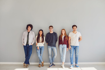 Group of young people in casual clothes smiling while standing against gray background. - Powered by Adobe