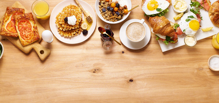 Brunch flatlay on wooden table. Healthy sunday breakfast with croissants, waffles, granola and sandwiches. Banner composition with copy space