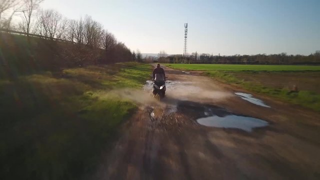 Aerial man on mega scooter water puddle without helmet countryside background
