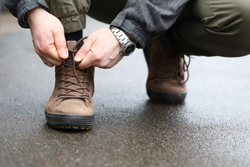 Close-up view of male hands sitting down outside on street and tying shoelaces on sneakers. Person lacing up stylish shoes. Sport walking and running concept