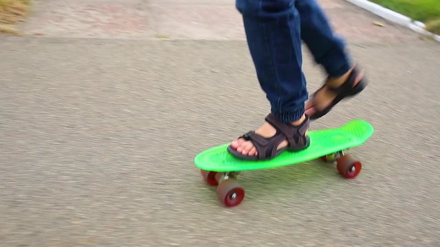 White child learning to skate on green plastic penny board in city street. Video of yong kid of 10 years has fun on summer or autumn evening.