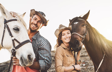 Happy couple having fun with horses inside stable - Young farmers sharing time with animals in...