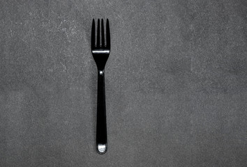 simple clean black plastic fork on a flat clean gray background with a hard shadow. The minimalist...