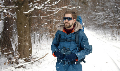 Fototapeta na wymiar Manly adult hiker in mirrored sunglasses walking alone in winter forest holding binocs, front view
