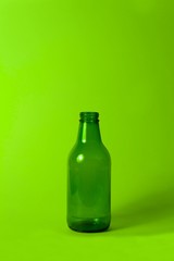 Small empty green glass bottle without cover and label on bright neon green background. Can be used as mock up for juice or beer.