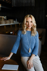 Fototapeta na wymiar Business portrait of an attractive beautiful blonde woman in a blue jacket and white trousers in a cafe restaurant, a girl working , drinking coffee, talking on the phone, freelancing