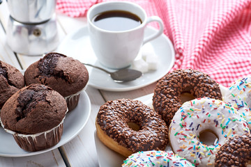Sweet breakfast with chocolate muffins and donuts, cup of black coffee on white wooden board table....