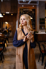 Beautiful attractive cute serious girl blonde freelancer sitting drinking coffee, working, talking on the phone, reading a newspaper in a cozy coffee shop in the loft style , portrait of a businesswom
