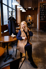 Fototapeta na wymiar Beautiful attractive cute serious girl blonde freelancer sitting drinking coffee, working, talking on the phone, reading a newspaper in a cozy coffee shop in the loft style , portrait of a businesswom