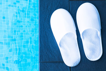 Composition with disposable white house woven slippers in a spa hotel near swimming pool, water. Spa, vacation, resort, relax, relaxation concept. Copy space. Bed shoes. Flat lay.