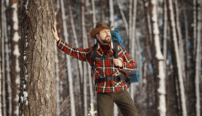 Adult bristled backpacker in stetson and with hiking gear enjoying winter scenery, selective focus