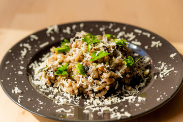 close up of fresh homemade italian mushroom risotto on wooden table with soft natural light with parmesan cheese and parsley leaves