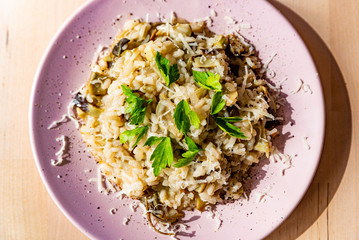 close up of fresh homemade italian artichokes risotto on wooden table with soft natural light and wine glass with parmesan cheese and parsley leaves