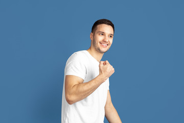 Fototapeta premium Winner, strong. Caucasian young man's portrait isolated on blue studio background. Beautiful male model in casual style, pastel colors. Concept of human emotions, facial expression, sales, ad.