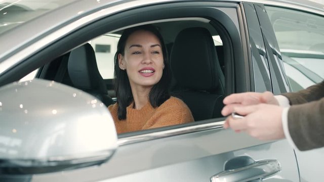 Happy young woman is getting key fob from salesman in automobile showroom buying car enjoying purchase. Business, deals and positive emotions concept.