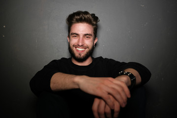 young handsome male with beard, mustache and trendy hairdo, wears casual grey sweater, has serious...