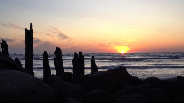 Abandoned old pier stones and logs and orange sunset on background