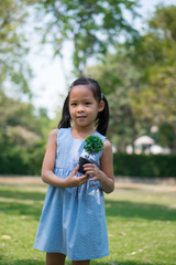 little girl holding small artificial plant in a garden