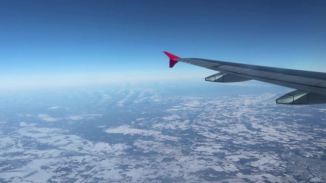 Traveling by airplane above the snowy ground.  Bright blue sky and airplane wing in frame.  Stationed camera looking out a window, slow movement.