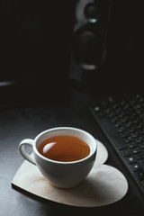Blurry image of white cup of tea and wooden plate on black desk