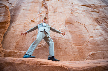 Nervous businessman balancing on a narrow ledge in a red rock canyon