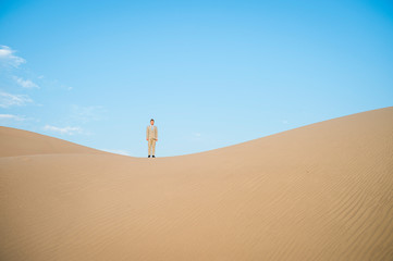 Fototapeta na wymiar Distant businessman standing on the ridge of a large desert sand dune 