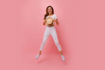 Inspired european young woman dancing in studio and laughing. Winsome brunette girl in white jeans and white t shirt jumping on pink background.