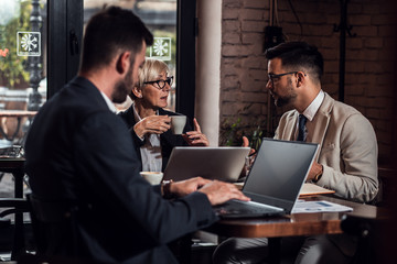 Senior businesswoman holding a casual meeting with her younger colleagues in coffee shop.
