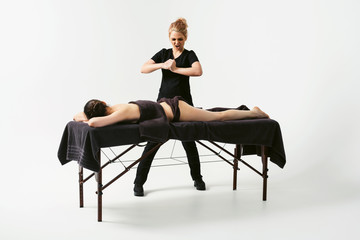 Funny fat burning massage. Portrait of cheerful woman masseur in uniforme near massage table with woman patient in wellness center. White background isolated