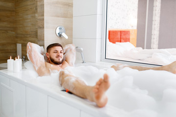 Man lying in bath with foam in the morning