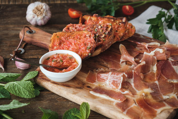 Meat platter with prosciutto and tomato dip on bread on wooden table with ingredients around