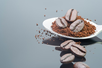 piled harmony coffee bean roast and ground coffee in spoon on shiny black backgrounds with shadow reflexing