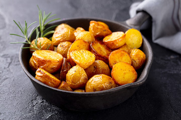 Roasted baby potatoes in iron skillet. Dark grey background. Close up.
