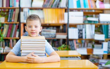 Single dreaming boy at the desk in the library enjoy books. European boy explore books. Pupil loves lecture, education, preparing for school.