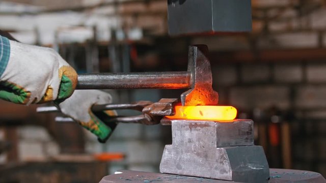 Blacksmith cutting the piece of hot metal with an axe and industrial forging pressure machine