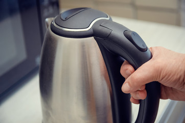 Hand of an elderly woman holding an electric kettle close-up, copy space
