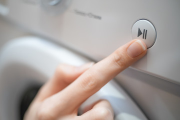 girl's hand presses the Start, Pause button on the control panel of the washing machine close-up