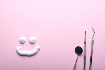 Stainless steel dental instruments and a toothpaste smiling face on pink background.