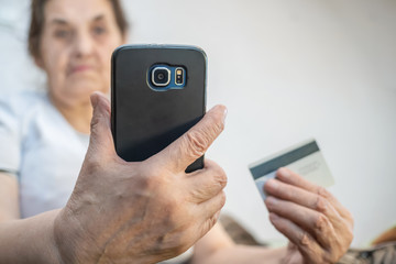 elderly woman is holding a mobile phone and a close-up card. Internet, innovative payment technologies, happy retirement, active lifestyle of the elderly