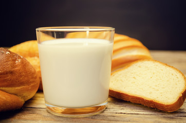 glass of milk in close-up, with fresh buns and a loaf in the background. Copy space