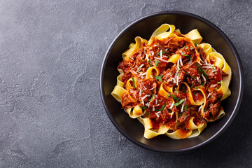 Pasta pappardelle with beef ragout sauce in black bowl. Grey background. Copy space. Top view. - 328040272