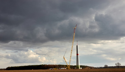 Fototapeta premium Construction of a wind turbine with an enormous crane, dramatic grey clouds in the background